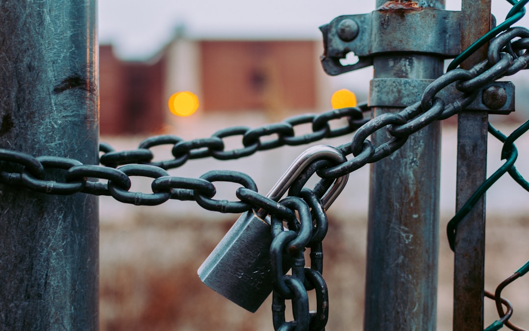 A close-up of a metal chain and padlock securing a gate, symbolizing the robust security offered by WordPress Hosting, with blurred buildings and orange lights glowing in the background.